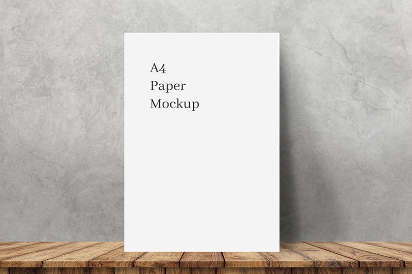 A4 Paper Mockup on Wooden Surface Against Concrete Wall