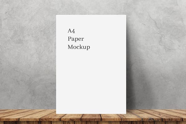A4 Paper Mockup on Wooden Surface Against Concrete Wall
